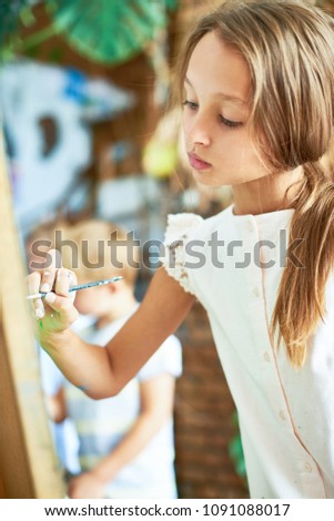 Portrait of talented pretty girl painting picture on easel in art class of development school