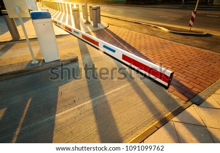 Close up of automatic boom barrier gate entrance illuminated by warm sunset light. Perspective view with long shadows