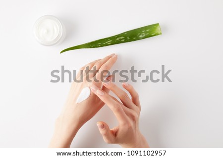 cropped shot of woman applying organic cream on hands, aloe vera leaf and cream container on white surface Royalty-Free Stock Photo #1091102957