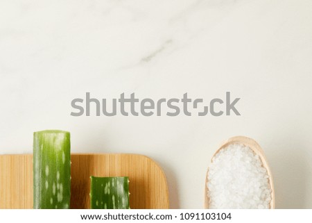 elevated view of aloe vera leaves on cutting board and wooden spoon with salt on marble table