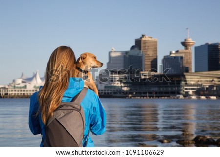 Girl holding her little dog, Chihuahua, and enjoying the beautiful view of the downtown city. Taken in Stanley Park, Vancouver, British Columbia, Canada.