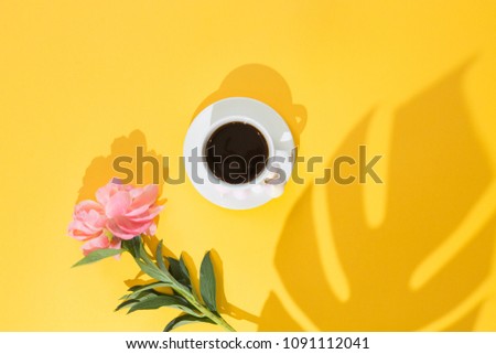 Top view of morning cup of coffee and a beautiful peony flowers on yellow summer background, flat lay.