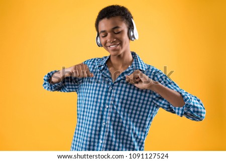 Afro American teenager in headphones is dancing. Isolated on yellow background. Studio portrait.
