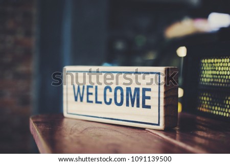 A wooden sign reads "Welcome" on a wooden table in a coffee shop.Vintage color style