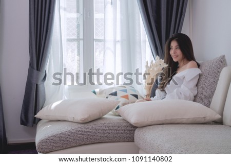 young asian woman smelling dry rabbit tail flowers on bed at living room, concept of asian woman sweetheart.