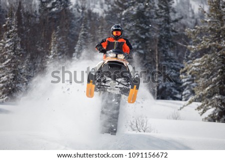 the guy is flying and jumping on a snowmobile on a background of winter forest  leaving a trail of splashes of white snow. bright snowmobile and suit without brands. extra high quality Royalty-Free Stock Photo #1091156672
