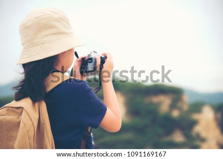 Happy smiling caucasian children asian girl backpack and  holding camera for take a photo check in on mountain.   Travel Concept.