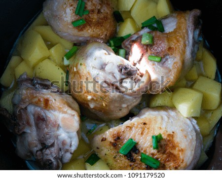 Roast chicken pieces with green onion and potatoes in the process of cooking 
