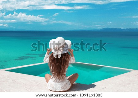 Carefree Woman relaxing in infinity swimming pool looking at view. Luxury resort. Beautiful destination summer vactions. Back view of traveller girl in beach hat and white bikini relax on Maldives.