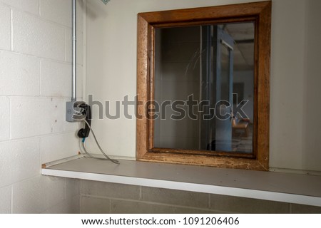 Phone next to window used by visitors to prison to communicate with inmates behind glass. Royalty-Free Stock Photo #1091206406