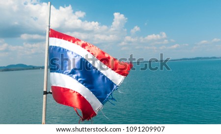 Thai flag waving in the wind with blue sky and beautiful sea.
