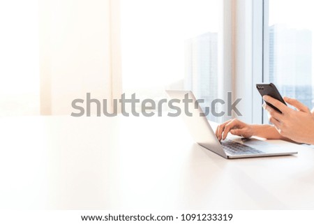 Businessman hand using laptop and mobile phone enjoying him online success, large windows outside building, city, tower view, soft focus