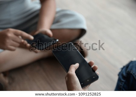 Two people holding a phone sitting on a gray background.