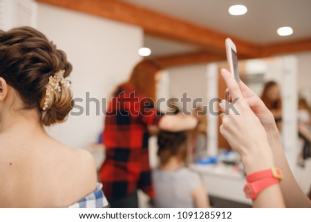 Hairdresser takes pictures of woman phone with finished hairstyle high beam on light background