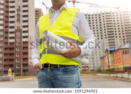 Closeup photo of male architect with blueprints posing against new buildings