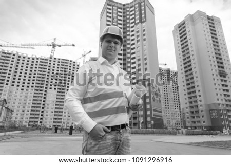 Black and white photo of architect with blueprints standing on building site
