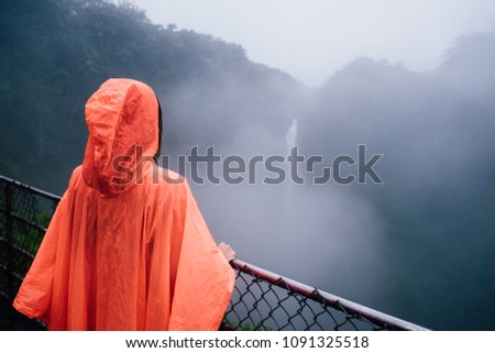 woman in rain coat is looking at waterfall in Hawaii 