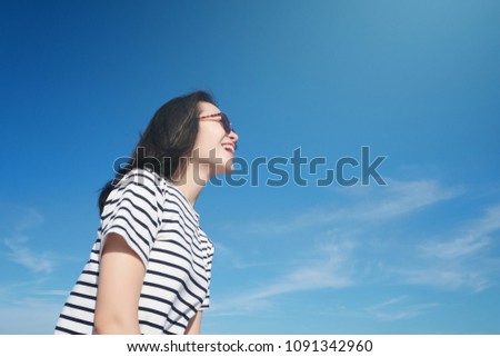 Portrait of a cute asian teenager young woman stand against blue sky and cloud. wearing sunglasses. wind blows hair. process to natural tone picture style. soft focus. hipster image. sun block concept
