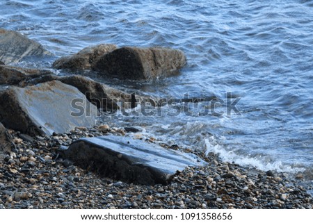 Gentle waves lapping against small rocks on a peddle beach on a sunny day.