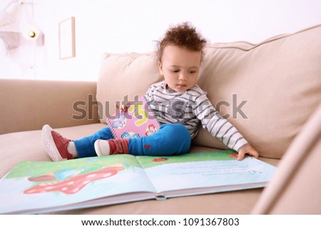 Cute little child with colorful book on sofa at home