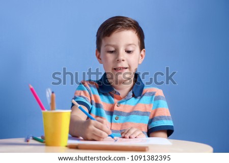 Cheerful smiling Caucasian boy spending time drawing with colorful pencils. 