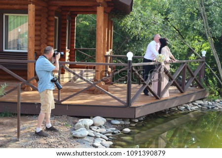 professional photographer takes pictures of a beautiful couple of newlyweds on the background of a cozy wooden house in the park.