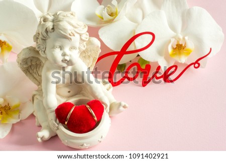 White Orchid angel sculpture wedding rings on pink background.