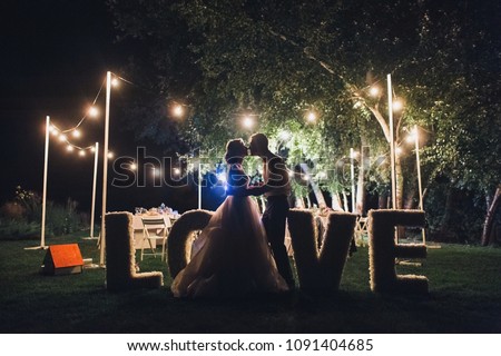 Beautiful newlyweds kiss tenderly at a wedding party with lamps. Stylish wedding ceremony. Love in the frame. Designer letters. Grain, film effect. Royalty-Free Stock Photo #1091404685