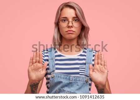 Serious beautiful female keeps palms in front shows rejection and refusal, wears casual clothes, isolated over pink background. Lovely woman journalist makes stop sign, doesn`t want to make interview