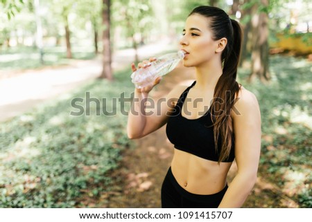 Beautiful athletic woman running in a park and drinking water