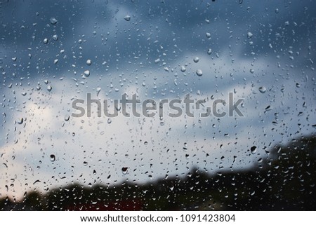 raindrops on a window with view to trees and blue cloudy sky
