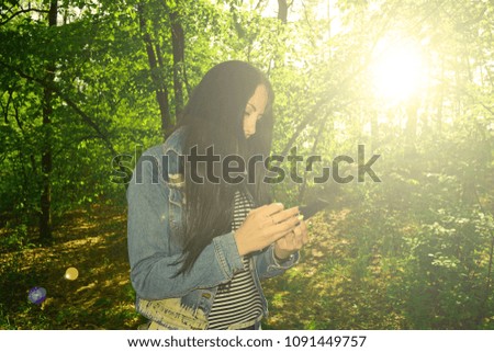 Brunette girl holding her mobile phone in the forest at dawn

