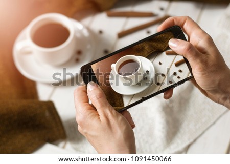 A woman's hand with a photo of a delicious breakfast with a coffee smartphone close-up. The blogger shares photos in social networks.