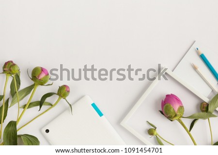Top view with copy space white table with  tablet, white photo frame, pencil and pink peony bud. Summer concept.