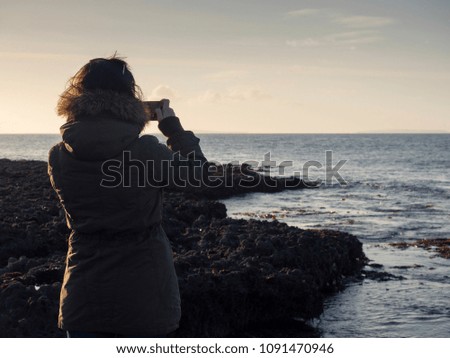 Woman taking picture of the ocean on her mobile phone. 