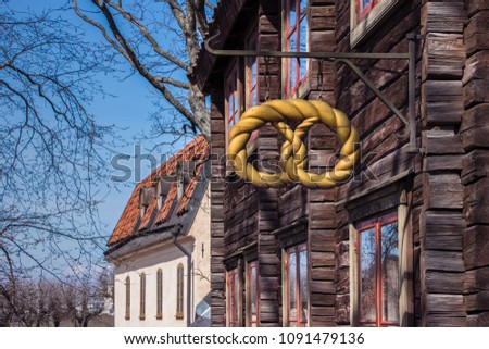 Golden pretzel outside a baker shop. Old bakery sign on a street of Stockholm, Sweden.  View on beautiful old store sign with wooden and stone buildings and blue sky on background. Spring sunny day. 
