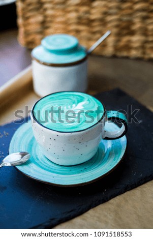 On the table there is a cup of blue coffee and a sugar bowl. Colorful coffee.