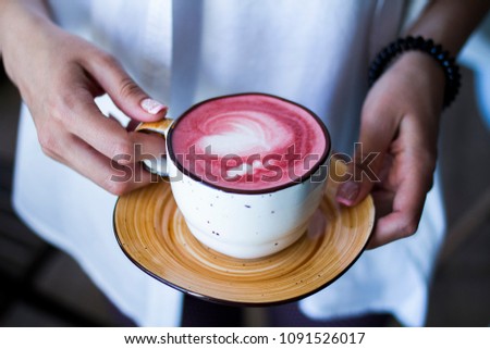 In female hands a cup of red coffee. On the foam painted heart.