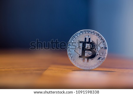 Cryptocurrency symbol electronic sign, focus on silver metal Bitcoin stack on wooden table, blur dark blue wall background copy space. Concept of transfer or exchange digital money through blockchain.