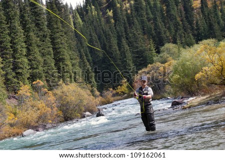 fly fishing angler makes cast while standing in water Royalty-Free Stock Photo #109162061