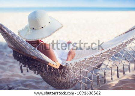 Young lady reading a book in hammock on tropical sandy beach