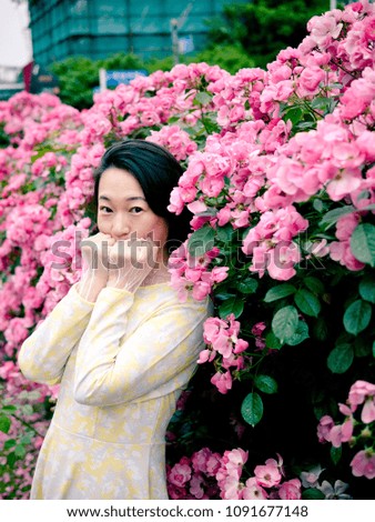 Outdoor portrait of beautiful young Chinese woman in yellow dress smiling among pink rose flowers wall in spring garden.