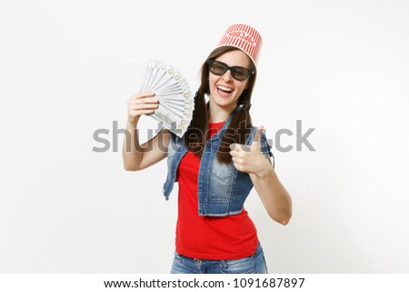 Young smiling pretty woman in 3d glasses with bucket for popcorn on head watching movie film, holding bundle of dollars, cash money, showing thumb up isolated on white background. Emotions in cinema