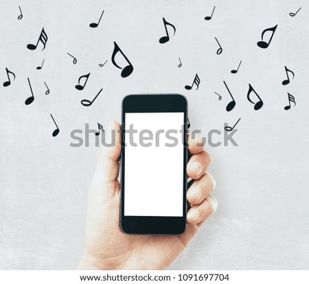 Hand holding empty white smartphone on concrete wall background with notes. Music concept. Mock up 