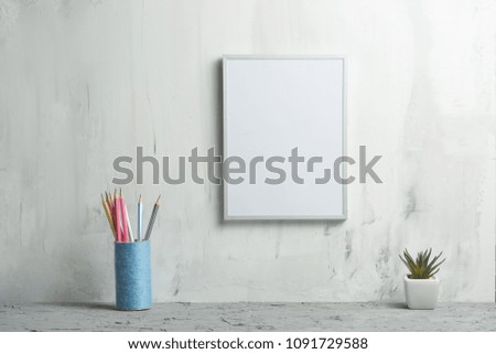Empty white frame with a flower with pencils against the wall background. The concept of design and font inscriptions and image placement