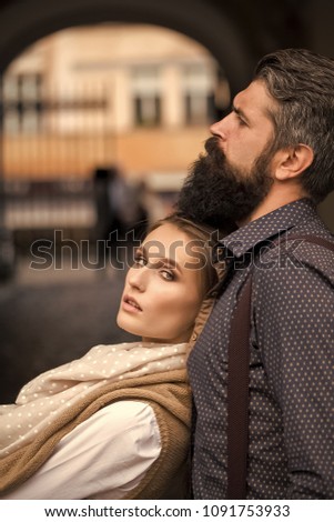 Beautiful stylish couple of young woman and man with long black beard standing embracing close to each other outdoor in autumn street near arch, vertical picture