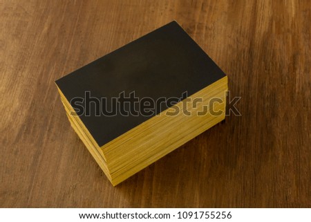 A mockup for a stack of black business cards with gold painted edges on a rustic background, with a place for text