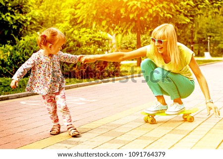 Beautiful smiling emotional mother with her daughter riding a skateboard in the park. Ekstrim