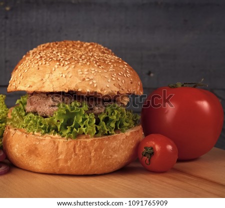 Big tasty appetizing fresh burger of green lettuce cheese bacon slice meat cutlet and white bread bun with sesame seeds and potato chips on wooden table closeup, square picture