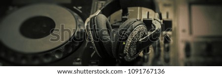 Closeup of glamour headphones with pastes and dj musical mixer professional console black color with many buttons and knobs in night club or studio on digital background, horizontal picture